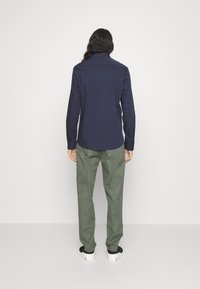 Camicia blu navy con maniche lunghe, abbinata a pantaloni verde chiaro. La camicia ha un colletto e un orlo dritto; i pantaloni hanno una vestibilità rilassata.