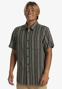 Camisa de manga corta en un patrón geométrico en blanco y negro, con cuello abotonado y bolsillo en el pecho, hecha de una tela ligera.