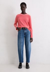 Rot-weiß gestreiftes Langarmshirt mit Rundhalsausschnitt, kombiniert mit hoch taillierten blauen Jeans und schwarzen Schuhen. Einfaches, lässiges Outfit.