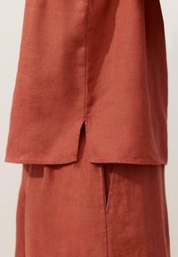 Oberteil und Hose aus leinenstoff in rostfarbener Optik mit Seitenschlitzen, die die Textur und saubere Nahtverarbeitung zeigen.