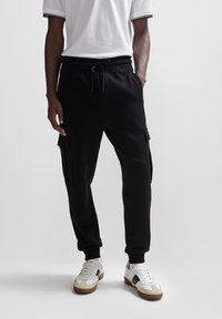 Svarta joggingbyxor i mjukt tyg, med elastisk midja och sidofickor. Matchas med vita sneakers och en grå T-shirt.