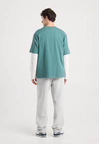 Vaatteet, joissa on lyhyet tealsävyiset hihat, kerroksittain pitkähihainen valkoinen paita, harmaat collegehousut sekä mustat ja harmaat lenkkarit.