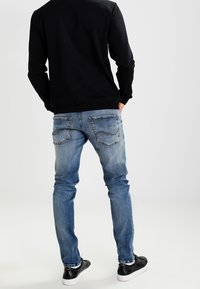 Modré džíny z denimu s úzkým střihem, se zadními kapsami zdobenými prošitím. Kombinovány s černými teniskami a černou mikinou.