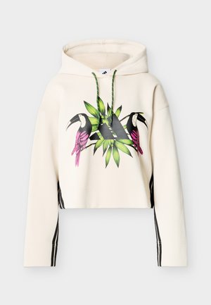 Μπεζ φούτερ με κουκούλα με πράσινα κορδόνια, μαύρο λογότυπο Adidas, απεικόνιση με ροζ τουκάν και πράσινα φύλλα στο μπροστινό μέρος, μαύρες ρίγες στα μανίκια.