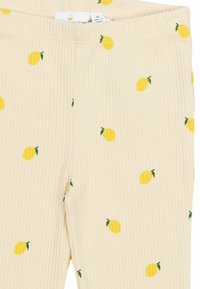Ριπ leggings σε ανοιχτό μπεζ με σχέδιο από μικρά κίτρινα λεμόνια και πράσινα φύλλα, με ελαστική μέση για άνεση.