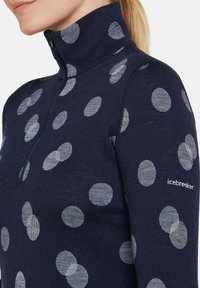 Navy Pullover mit einem halben Reißverschluss-Kragen, der unterschiedlich große graue Punkte zeigt. Das Material ist gestrickt, mit einer glatten Textur und dem Markenlogo auf dem Ärmel.