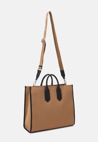 Brązowa torba tote z czarnymi uchwytami i brzegami, regulowany pasek na ramię z wytłoczonym tekstem, stojąca na białym tle.