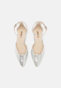 Ballerine metalliche argento con punta affusolata e cinturini alla caviglia. Texture liscia, design minimalista, con soletta beige e dettaglio della fibbia.