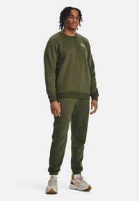 Olivenfarget fleecegenser og matchende joggebukser, med rund hals, ribbet mansjetter og en liten logo på brystet. Avslappet passform.