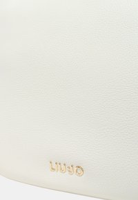 Witte gestructureerde synthetische handtas met een in goud embossed logo. Heeft een gladde afwerking en een gebogen vorm, geschikt voor casual gebruik.