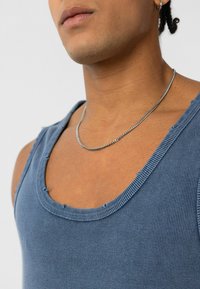Blauw geribde tanktop met een wijde halslijn, voorzien van versleten randen en een gladde textuur. Gecombineerd met een zilveren ketting.