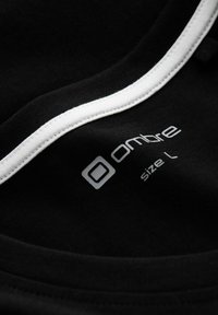 Černá látka s bílým lemováním u výstřihu, na které je zobrazeno logo značky "ombre" a velikost "L" v šedém písmu. Měkká textura, neformální design.