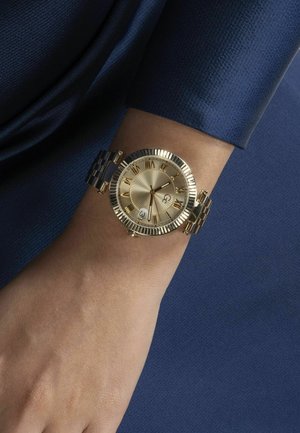 Guldtonet armbåndsur med en ribbet bezel, romerske talmarker, og en struktureret solstråledial. Sølvtonet metal link armbånd.