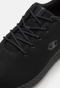 Scarpa atletica nera con una tomaia in mesh testurizzato, lacci rotondi e occhielli rinforzati. Presenta una suola in gomma distintiva per una migliore aderenza.