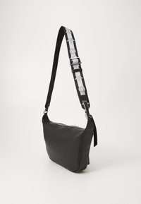 Borsa a tracolla in pelle nera con una larga tracolla regolabile, decorata con motivi di stelle e cerchi bianchi, e chiusura superiore a zip.