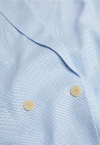 Tissu bleu clair texturé avec un petit motif à carreaux et deux boutons beige sur un vêtement avec col.