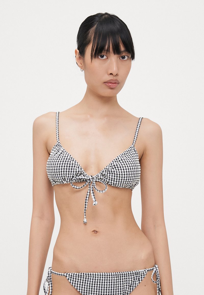 Zwart-wit geruite bikini, met een driehoekige top met een strik aan de voorkant en verstelbare bandjes. Het broekje heeft zijstrikjes. Glad textuur.