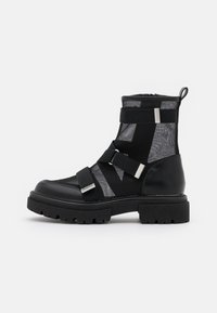 Svart ankelboot med chunky sula, mesh-paneler, tre justerbara remmar med silverfärgad spänne och en dragöppning baktill.