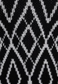 Tejido de punto con un patrón geométrico en blanco y negro que presenta formas de diamante. La textura es suave con un ligero estiramiento.