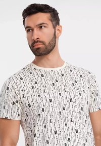 Hvid t-shirt med korte ærmer, der har et sort vertikalt tekstmønster med varierende skriftstørrelser og -stile. Blødt stof med rund halsudskæring.