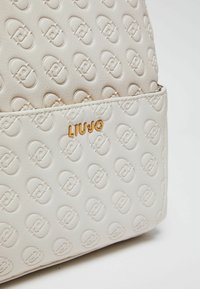 Borsa color crema con motivo a logo impresso ripetuto e piccolo nome del marchio LIU JO sulla tasca anteriore.
