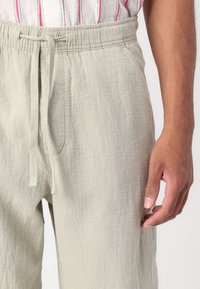 Light gray linen pants with an elastic waistband and drawstring, featuring a soft, textured finish and side pockets.