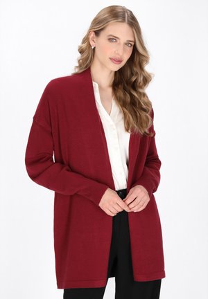 Dlouhý burgundský cardigan s otevřeným předním dílem, žebrovanými manžetami a měkkou texturou, nošený přes bílé košilové shirt a černé kalhoty.