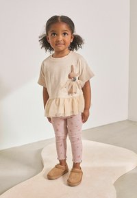 Beige topp fodros szegéllyel és nyuszi applikációval; rózsaszín csíkos leggings virágmintával; barna slip-on cipők. Sima anyag, játékos design.