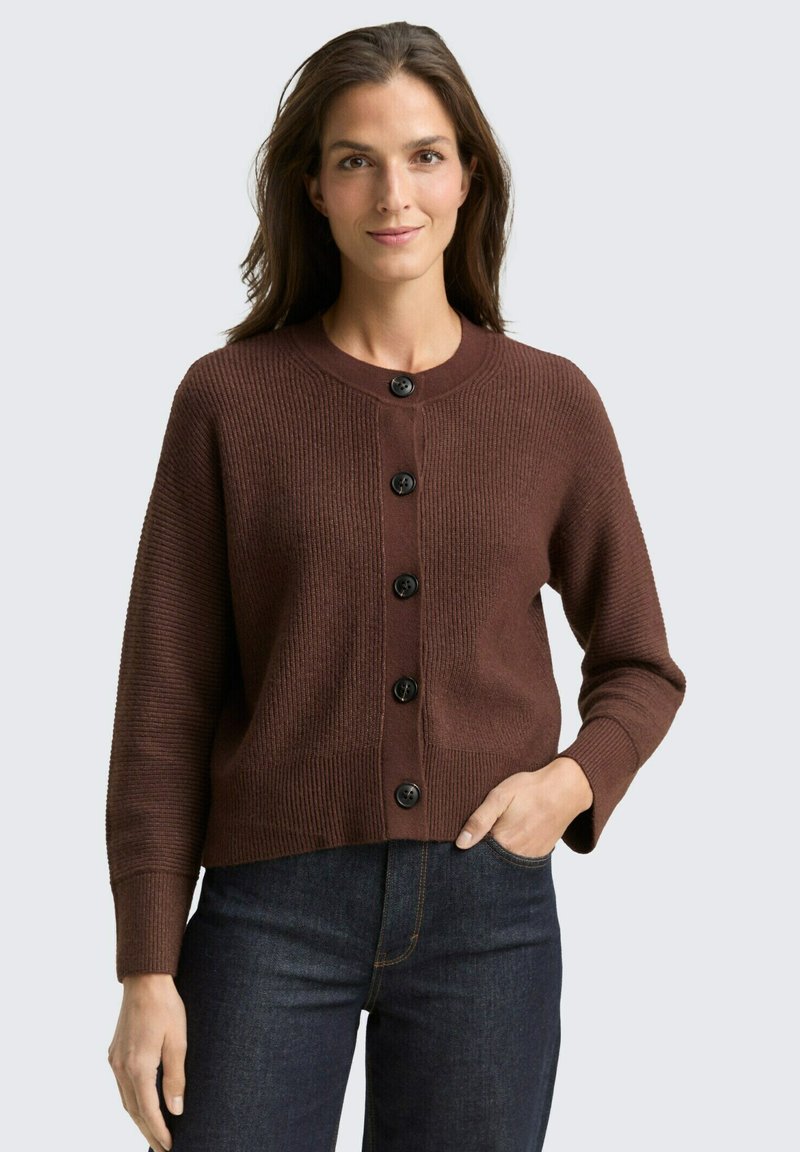 Brauner gerippter Cardigan mit rundem Halsausschnitt, schwarzen Knöpfen auf der Vorderseite und langen Ärmeln, kombiniert mit dunklen Jeans.