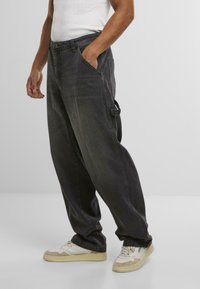Baggy zwarte denim broek met een hoge taille, grote zakken en een zachte textuur, gecombineerd met witte en beige sneakers.