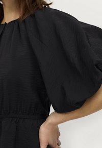 Black dress with a textured fabric, featuring puffed sleeves, an elastic waist, and a round neckline. Smooth finish with casual design.