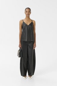 Top in pelle nera senza maniche con spalline sottili, abbinato a pantaloni larghi in pelle nera. Accentuato da una piccola borsa nera con borchie e tacchi color crema.