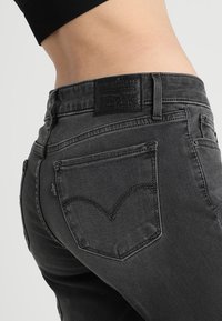 Grå denimjeans med hög midja, med bakfickor som har ett distinkt böjt sömnadsmönster och en läderetikett vid midjebandet.