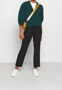 Turkusowy, dziergany kardigan, biały t-shirt, czarne spodnie i białe sneakersy. Torebka na ramię ze skórki w kolorze pomarańczowym z paskiem.