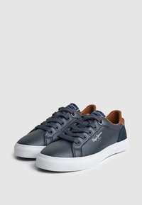 Pāra tumši zilu zemu virsēju sporta apavu ar baltu zolēm, tumši ziliem šņorēm un brūnu iekšējo odere, ar zīmolu "Pepe Jeans" uz sāniem un mēlītes.