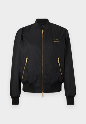 Černá bomber bunda s hladkou texturou, zlatými zipy a logem na hrudi. Má žebrované manžety a pas.