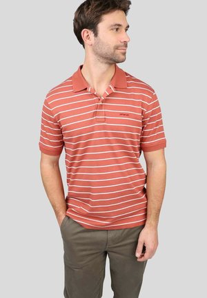 Polo rayé en rouille avec des rayures horizontales blanches, manches courtes, col et logo discret sur la poitrine. Porté avec un pantalon kaki.