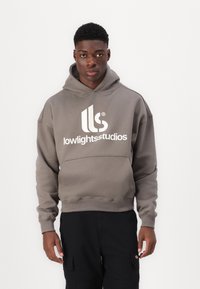 Gray hoodie with large white "lowlightstudios" logo, kangaroo pocket, ribbed cuffs, and hem. Worn with black cargo pants.