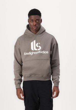 Sivi dukserica s velikim bijelim logotipom "lowlightstudios", kengurska džep, rebrasti rukavi i donji rub. Uparena s crnim cargo hlačama.