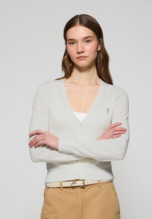 Cárdigan ligero color crema con un diseño de cuello en V, mangas largas y un pequeño logo bordado en el lado izquierdo. Fabricado con tela suave.