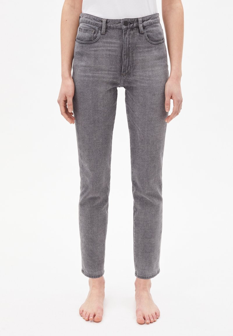 Jean en denim gris coupe droite porté pieds nus par une personne debout devant un fond blanc uni.
