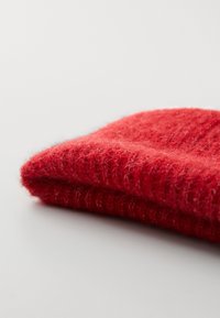 Punane kudumüts, mis on valmistatud pehmest villast, sisaldab tekstuurset mustrit ja painutatud äärt, andes sooja ja häärdamise välimuse.