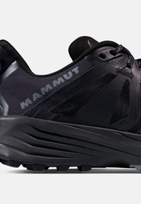 Chaussure de sport noire avec une tige en maille texturée, des accents réflecteurs et une semelle en caoutchouc striée pour l'adhérence. Marquage sur le côté.