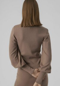 Maglione marrone lavorato a maglia con maniche lunghe a sbuffo e polsini a coste. Il tessuto appare morbido, aderente e dal design minimalista.
