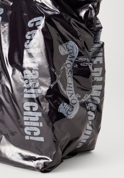 Geantă neagră lucioasă cu textul „C'est trash chici!” și „Moschino” imprimat în gri uzat. Prezintă o textură împăturită și accente grafice abstracte.