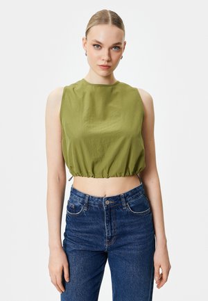 Top corto sin mangas en color caqui con un escote redondo y dobladillo fruncido, combinado con jeans de mezclilla azul de cintura alta. Textura de tela suave.