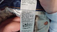 Etiqueta con instrucciones de cuidado en varios idiomas, detallando la composición de 100% algodón, junto con iconos para los métodos de lavado y secado.