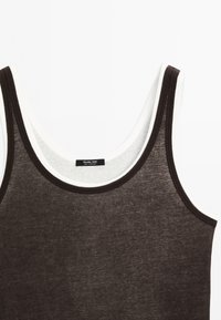 Hnědý top na ramínka s bílým lemem, vyrobený z měkké tkaniny, s kulatým výstřihem a širokými ramínky. Štítek viditelný uprostřed.