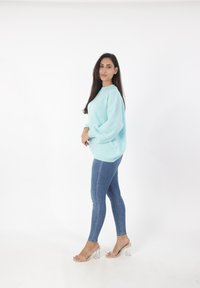 Maglione oversize azzurro chiaro con maniche a palloncino, abbinato a jeans in denim aderenti. Sandali con tacco a stiletto trasparenti completano l'outfit.