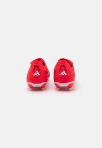 Red soccer cleats with textured upper, white sole, and black accents. Features include a low-cut design and signature logo on the heel.